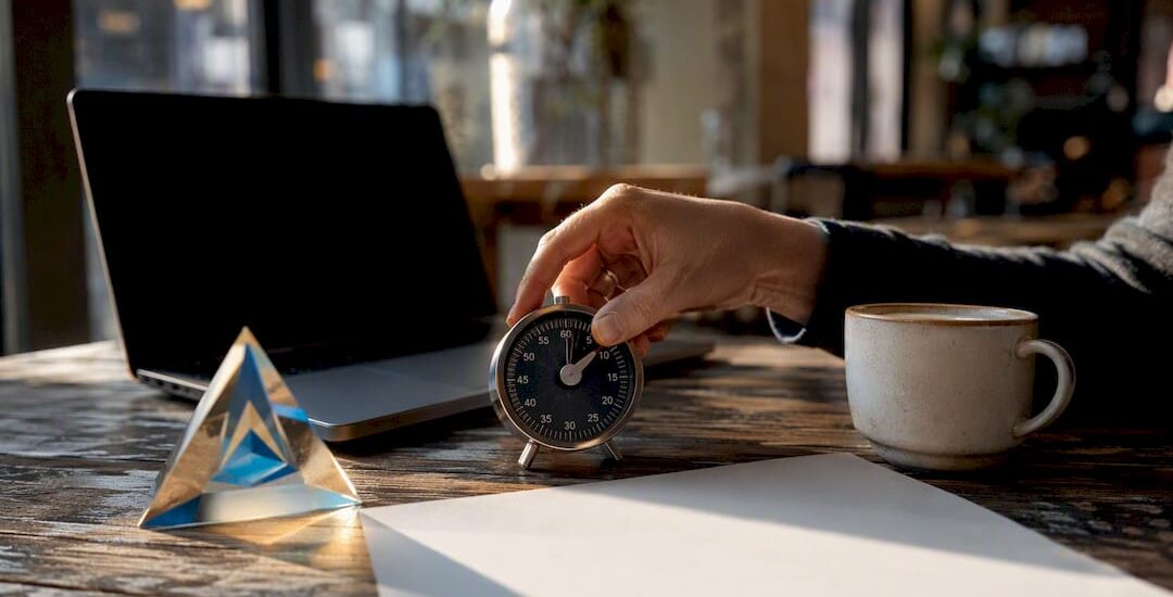 Hand adjusting timer beside Blue Prysm prism on desk