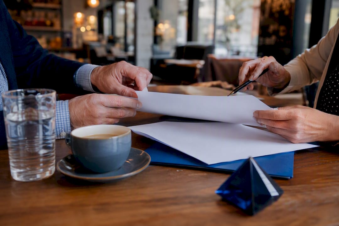 Hands exchanging project folders at meeting table